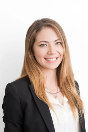 Smiling woman in a black blazer and white blouse shot against a bright white background, confident professional headshot.