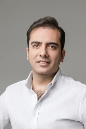 Smiling man in a white shirt against a soft gray backdrop, confident professional headshot with studio lighting.