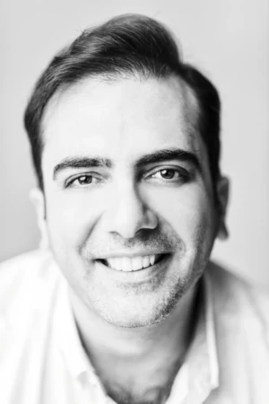 Black-and-white close-up of a smiling man in soft studio light, an authentic professional headshot for personal branding.