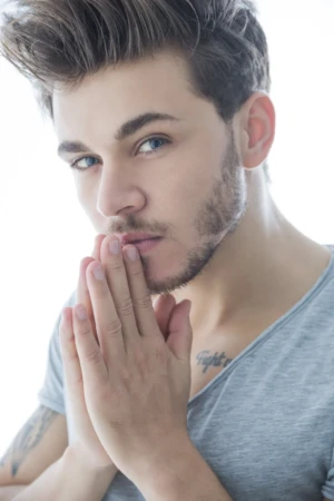 Expressive actor headshot of a contemplative young man in a grey tee, soft high-key studio portrait lighting.
