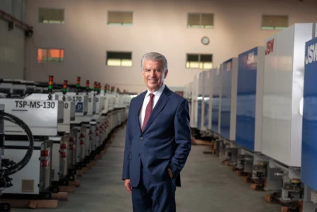 Smiling man in a navy suit poses amid factory machines under soft light, a professional executive portrait in Berlin.