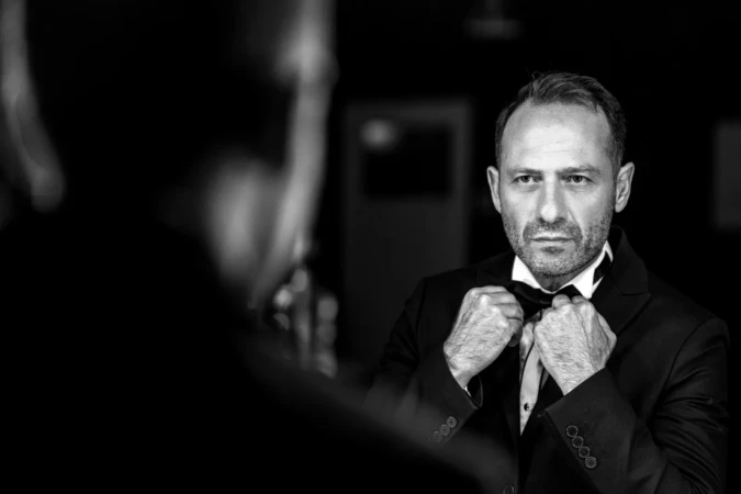 Serious mature man in a tux adjusting his bow tie, cinematic black-and-white professional headshot with studio lighting.