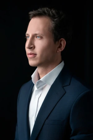 Studio portrait of a young man in a navy suit and white shirt looking confident, a professional business headshot.