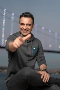 Smiling man in a gray hoodie reaches toward the camera against soft evening bokeh, an authentic personal branding photo.