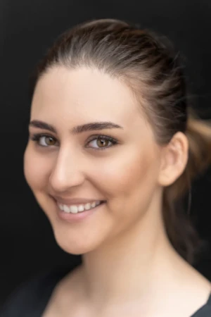 Smiling young woman in a close-up, softly lit studio professional headshot with an authentic, warm expression.