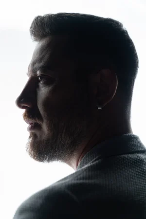 Backlit profile of a bearded man in a textured jacket, a cinematic studio portrait with dramatic rim lighting.