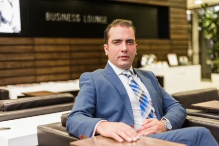 Man in blue suit seated in a softly lit business lounge, confident expression and polished business headshot.