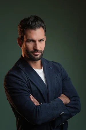 Confident man in a navy blazer looks into camera with arms crossed against a green backdrop, cinematic professional headshot.