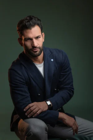 A bearded man in a navy blazer looks confidently at camera in a cinematic professional headshot with soft studio lighting.