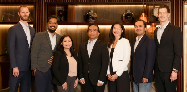 Seven executives pose smiling in warm wood-paneled lighting, a professional team portrait in Berlin.