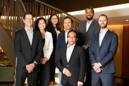 Seven professionals in business attire pose smiling on a lit staircase in a professional team portrait.