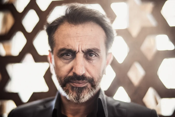 Cinematic professional portrait of a bearded man with an intense gaze, soft backlit geometric background.