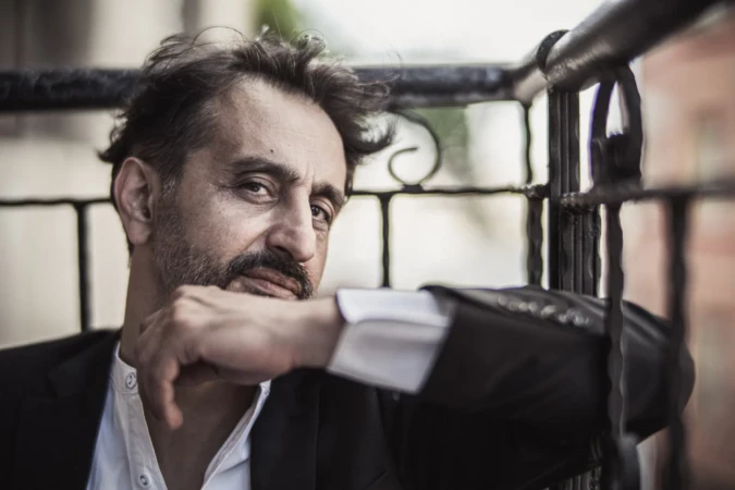 Moody close-up of a bearded man in a suit leaning on a railing, a cinematic actor headshot with soft natural light.