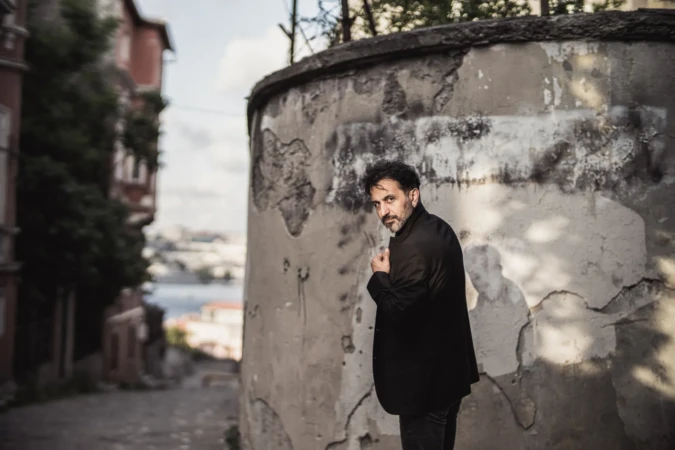 Bearded man in a dark coat looks over his shoulder by a weathered wall, cinematic personal branding photo