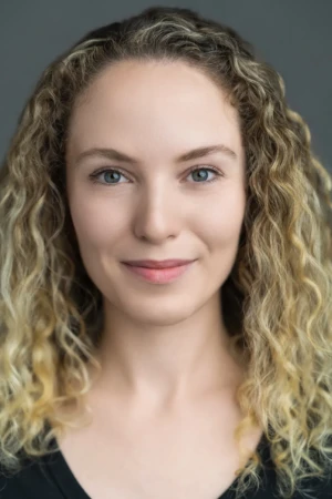 Close-up portrait of a smiling woman with curly blonde hair and soft lighting, a confident professional headshot.