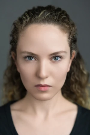 Close-up neutral actor headshot of a woman with curly hair and intense gaze in cinematic soft light.