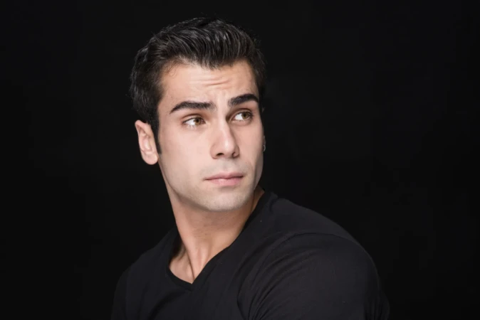 Young man in a black tee looks off-camera against a dark background in a cinematic actor headshot.