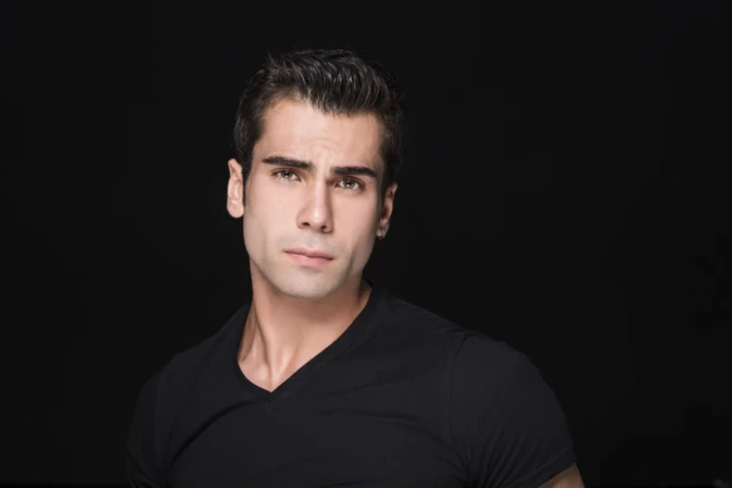 Studio-lit actor headshot of a serious young man in a black tee against a dark background, cinematic and striking.