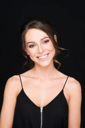 Smiling woman in a black top photographed against a black backdrop in an authentic studio portrait.