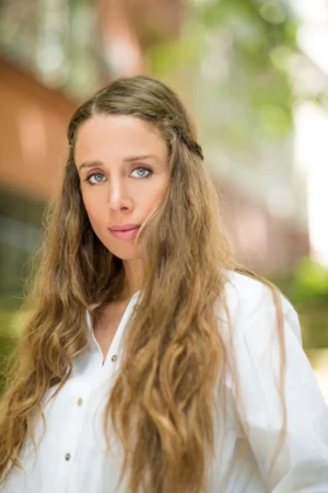 Outdoor actor headshot of a woman with long wavy hair and white blouse, authentic natural-light portrait.