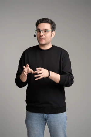 Man in glasses and headset gestures while speaking against a grey studio backdrop, an authentic personal branding photo.
