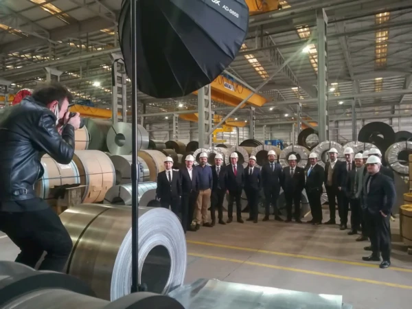 Photographer capturing an authentic team portrait of suited men in hard hats among steel coils in a warehouse.