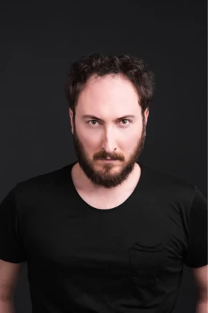 Actor headshot of a bearded man with an intense gaze in a black tee on a dark studio background, cinematic light.