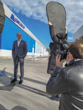 Man in a gray suit poses outside for a corporate headshot, photographer using reflector for natural light.