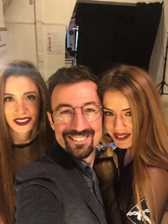 Close-up selfie of three smiling people in warm studio light, a man in glasses and two women; an authentic studio portrait.