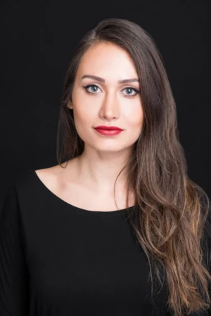 Close-up studio portrait of a composed woman with red lipstick and soft lighting, a confident professional headshot.