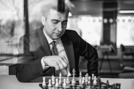 Business professional in a suit playing chess indoors, focusing intently on the game, conveying strategy and concentration.