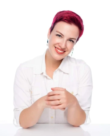 Smiling woman with short magenta hair in a white shirt against a bright studio background, a confident professional headshot.