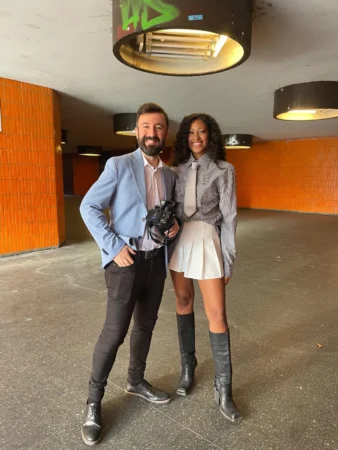 Two individuals pose in a vibrant underground space, showcasing a stylish aesthetic with orange tiled walls and industrial lighting.